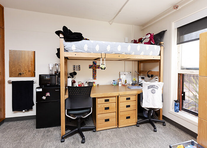 Interior shot of a bedroom in Stern Hall. A microwave sits atop a mini-fridge next to a lofted bed with desks underneath.