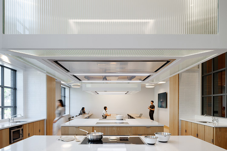 Several pots and bowls sit on the countertop and stove of the communal Pantry kitchen. Students sit at tables in the back of the room, talking to one another.